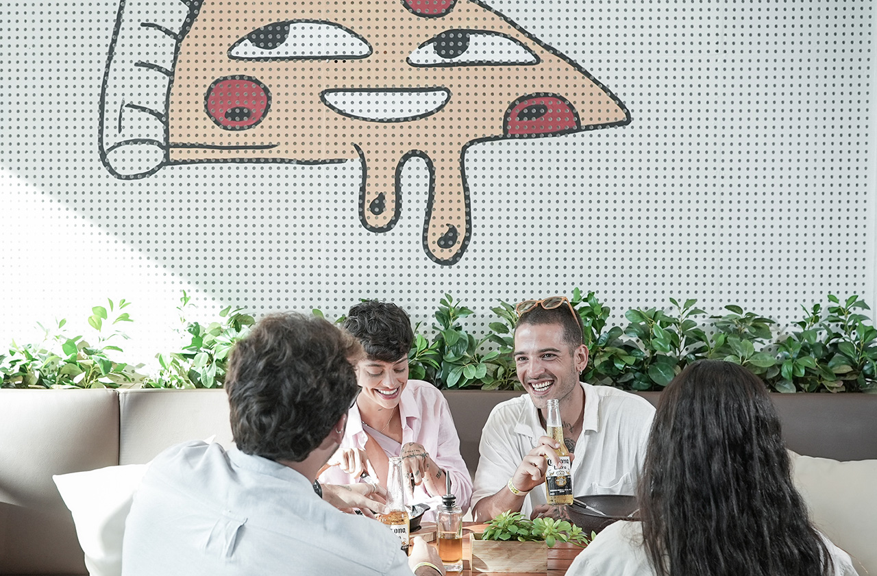 A imagem mostra a pizzaria Amore um ambiente jovial e moderno. Possui um grande mural colorido, com elementos gráficos estilizados que incluem alimentos, a frase 