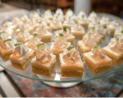 Prato de sobremesas pequenas, com topo de creme e fatias de limão, dispostas em um suporte de vidro no buffet do Restaurante Tabôa com cadeira ao fundo.